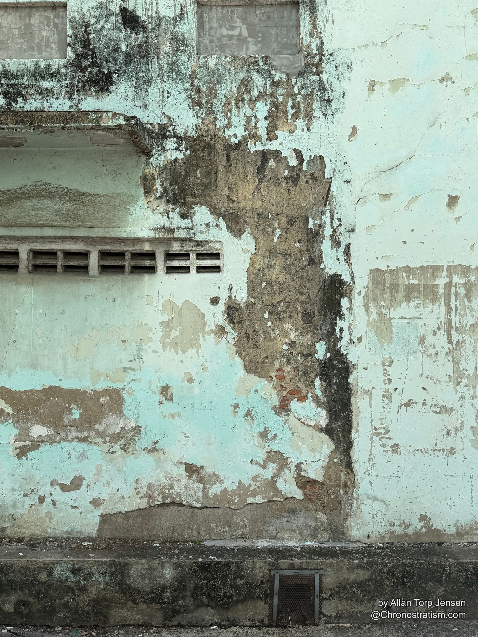 A wide shophouse facade shows peeling paint, dark mold and brick exposed around a vent.